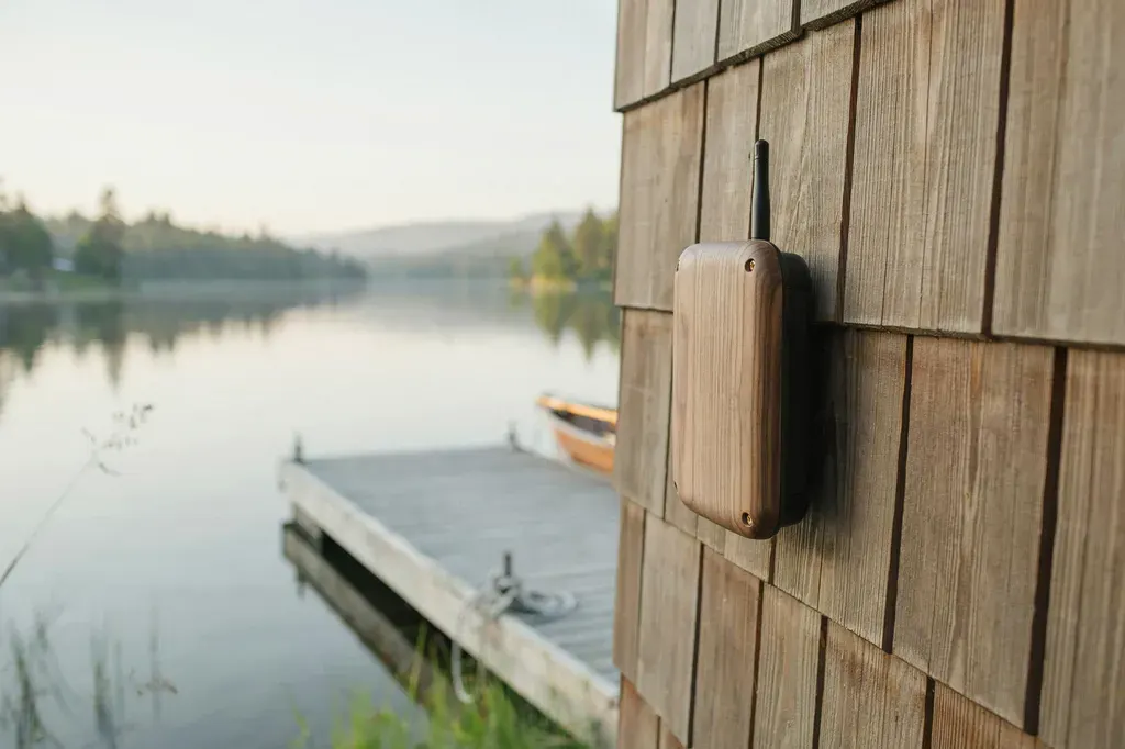 Concept of a hand-built outdoor sensor in wood and aluminum, mounted on a weathered post by the beach.