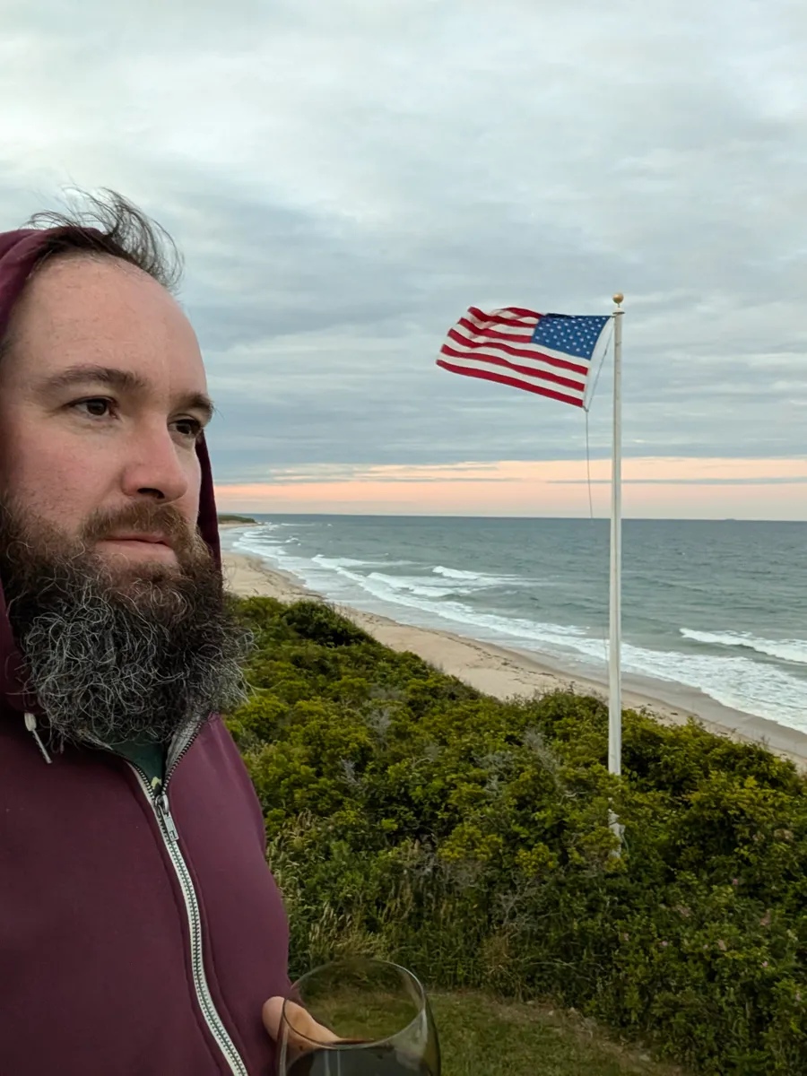 The maker on a coastal bluff at dusk, the sea and a flag behind him.